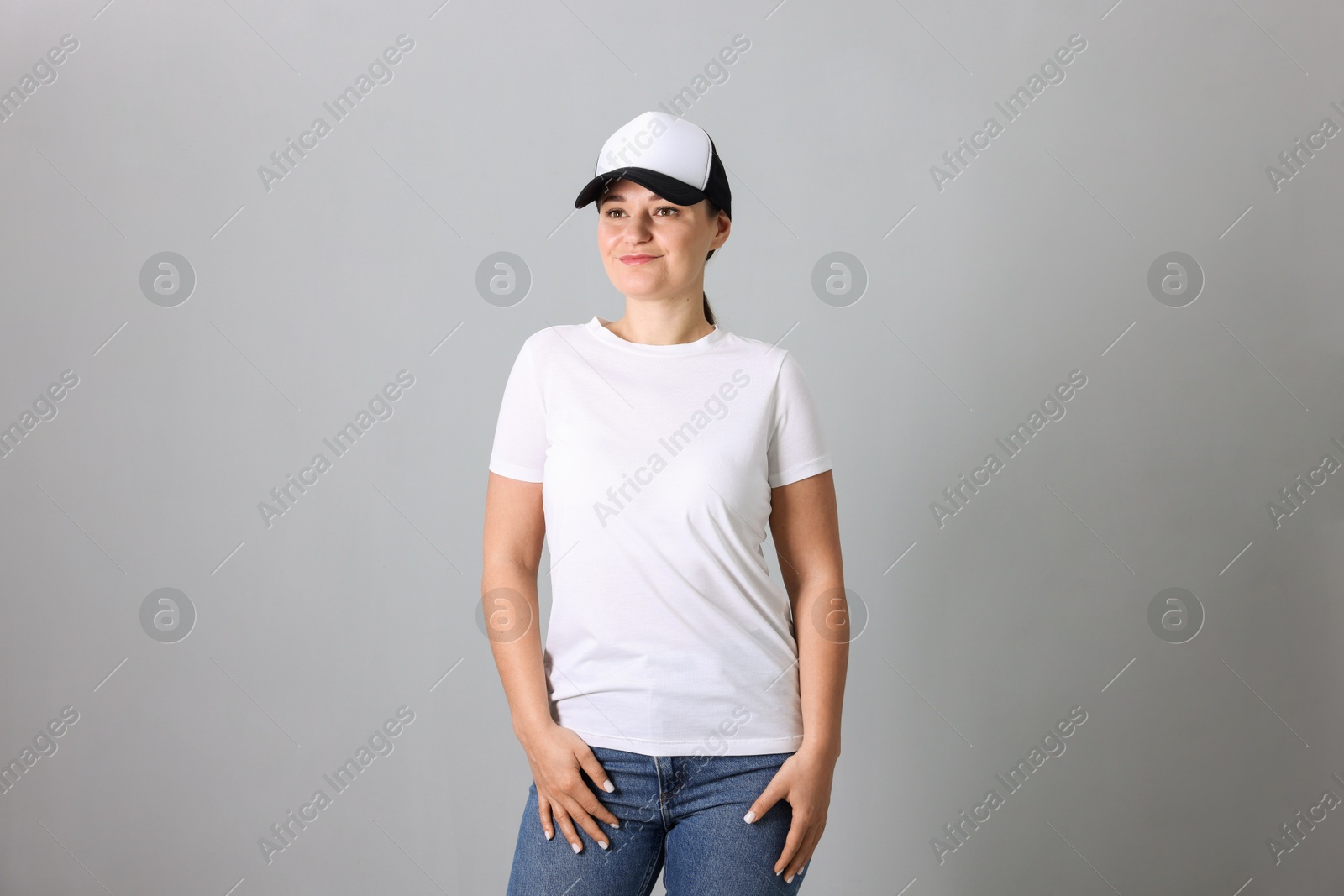 Photo of Woman in white t-shirt and baseball cap on grey background. Mockup for design