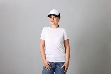 Photo of Woman in white t-shirt and baseball cap on grey background. Mockup for design