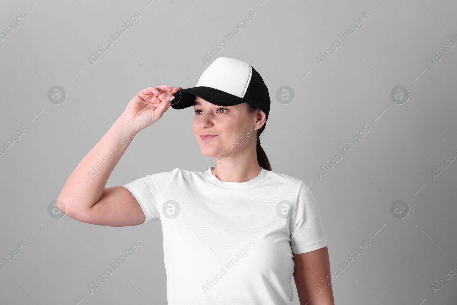 Photo of Woman in white t-shirt and baseball cap on grey background. Mockup for design