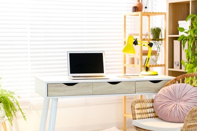 Photo of Home office. Comfortable workplace with laptop and lamp on desk indoors