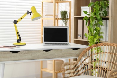 Photo of Home office. Comfortable workplace with laptop and lamp on desk indoors