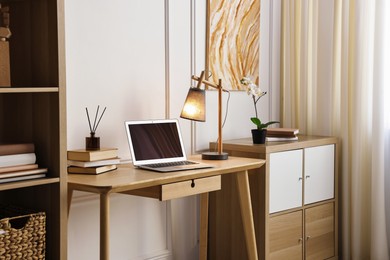 Photo of Comfortable workplace with modern laptop and lamp on wooden desk in home office