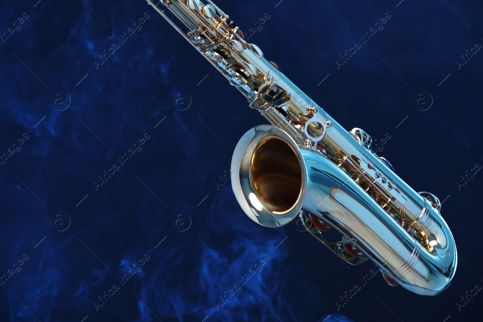 Photo of Golden saxophone on dark blue background with smoke, closeup. Space for text