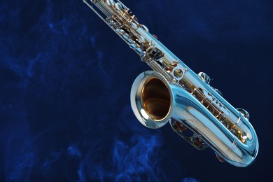 Golden saxophone on dark blue background with smoke, closeup. Space for text