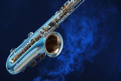 Photo of Golden saxophone on dark blue background with smoke, closeup. Space for text