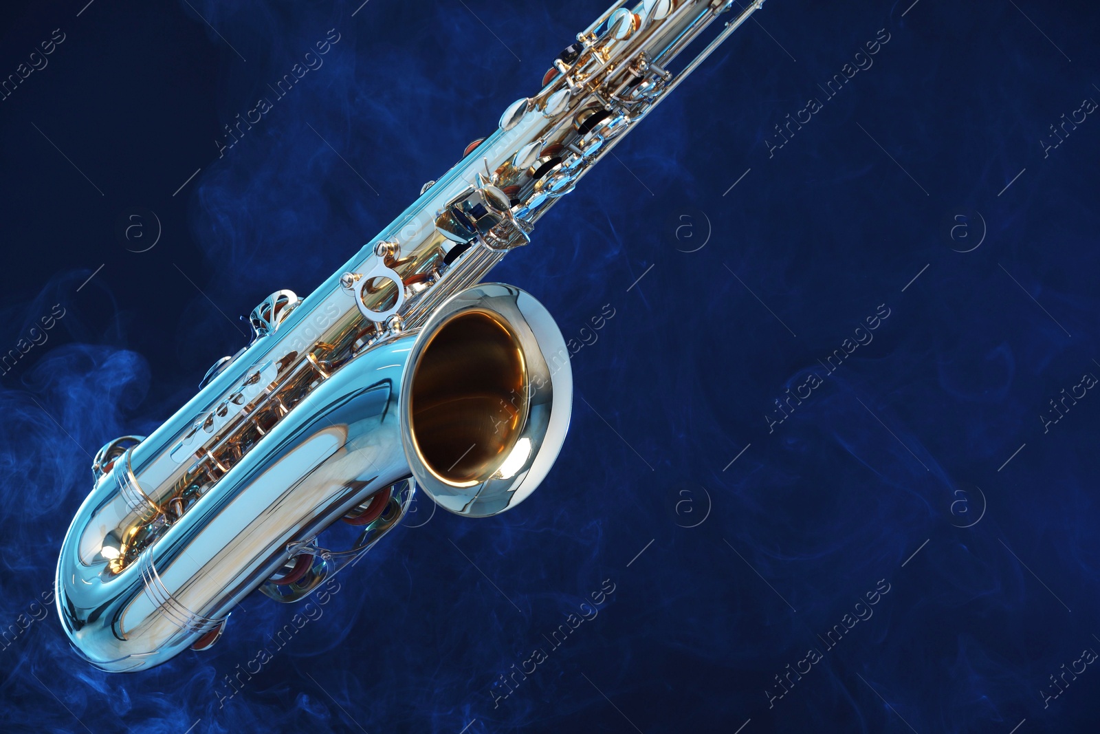 Photo of Golden saxophone on dark blue background with smoke, closeup. Space for text