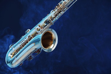 Golden saxophone on dark blue background with smoke, closeup. Space for text