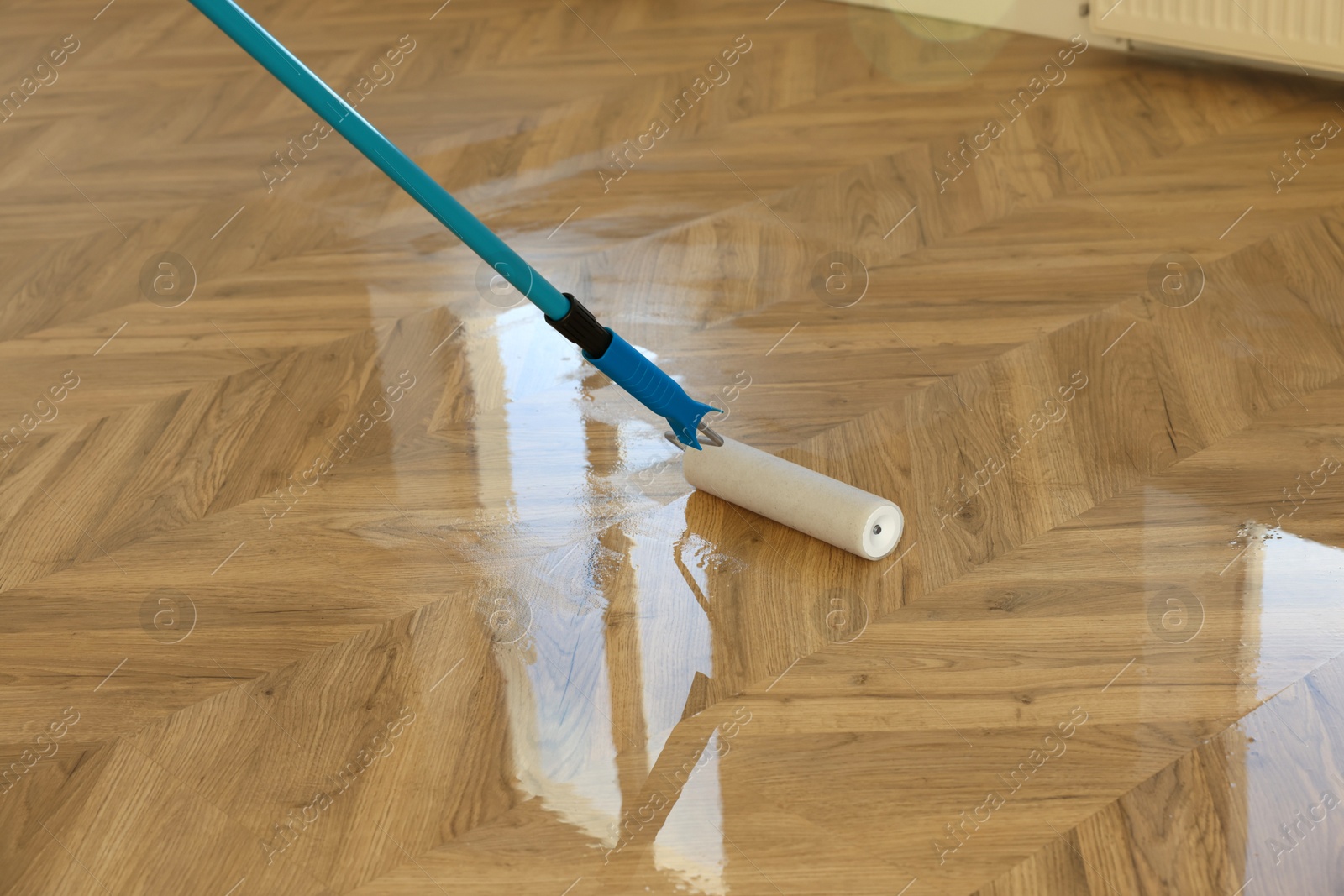 Photo of Polishing parquet with roller and varnish indoors, closeup