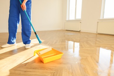 Photo of Process of polishing. Man dipping roller into tray with varnish indoors, closeup