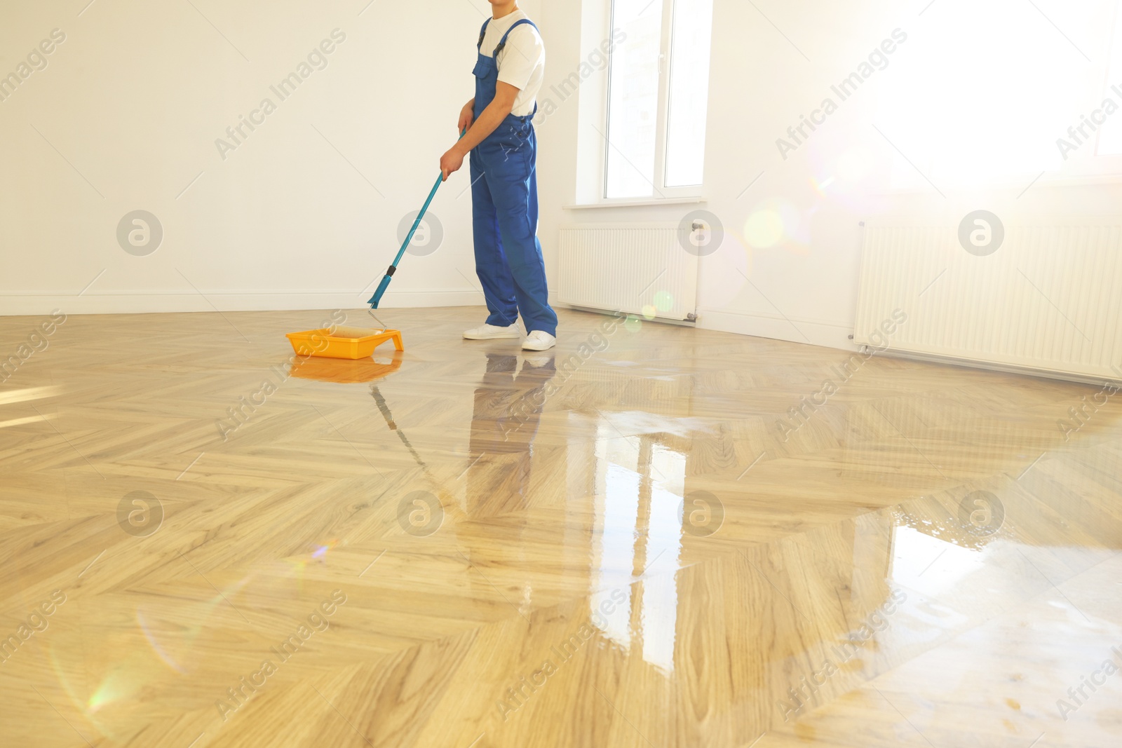 Photo of Process of polishing. Man dipping roller into tray with varnish indoors, closeup