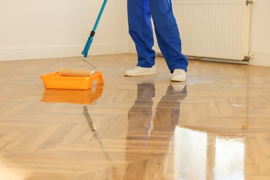 Process of polishing. Man dipping roller into tray with varnish indoors, closeup