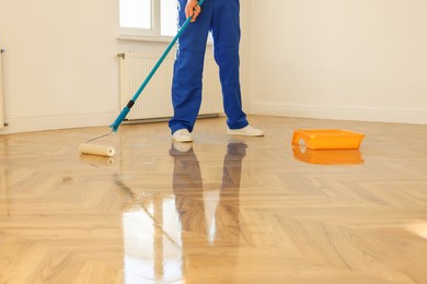 Photo of Man polishing parquet with varnish indoors, closeup