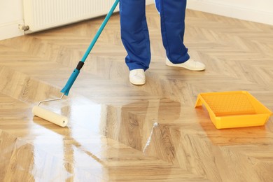 Photo of Man polishing parquet with varnish indoors, closeup