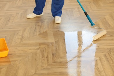 Photo of Man polishing parquet with varnish indoors, closeup