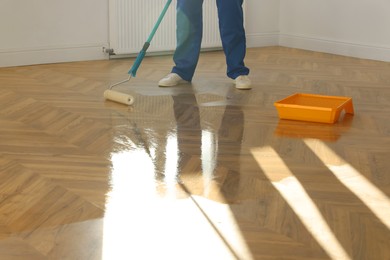 Photo of Man polishing parquet with varnish indoors, closeup