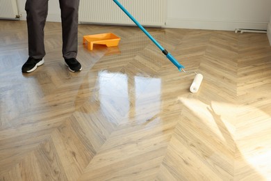 Photo of Man polishing parquet with varnish indoors, closeup