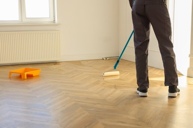 Photo of Man polishing parquet with varnish indoors, closeup