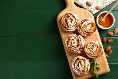 Photo of Tasty apple roses with powdered sugar served on green wooden table, flat lay. Space for text