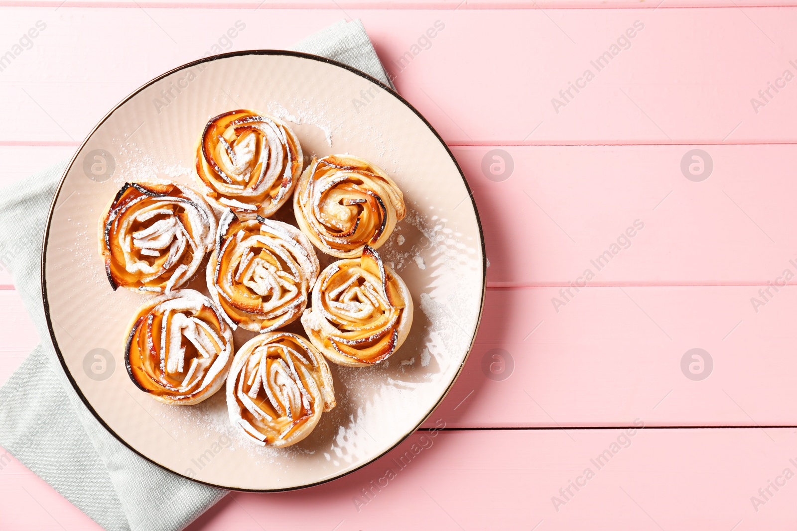 Photo of Tasty apple roses with powdered sugar on pink wooden table, top view. Space for text