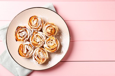 Photo of Tasty apple roses with powdered sugar on pink wooden table, top view. Space for text