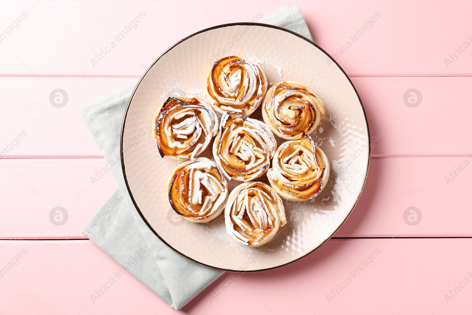 Photo of Tasty apple roses with powdered sugar on pink wooden table, top view