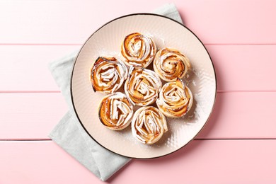 Photo of Tasty apple roses with powdered sugar on pink wooden table, top view