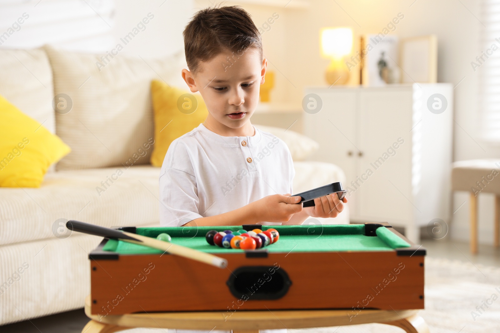 Photo of Cute little boy playing billiards at home