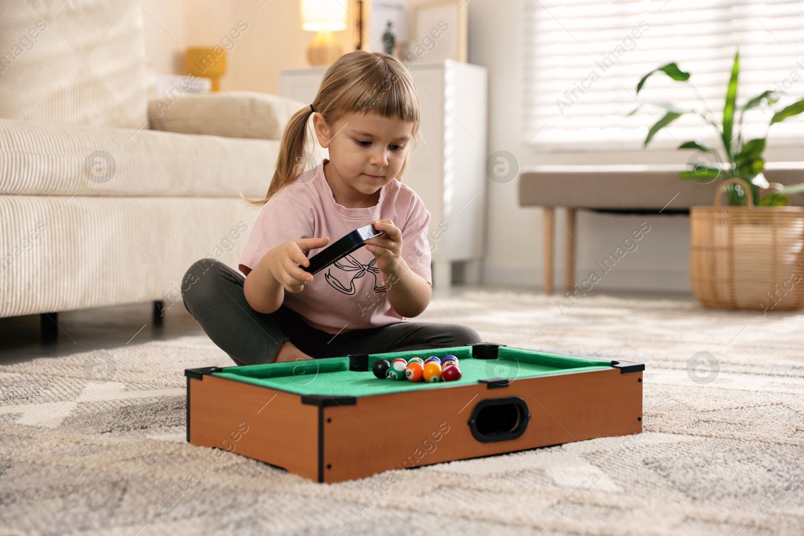 Photo of Cute little girl playing billiards at home