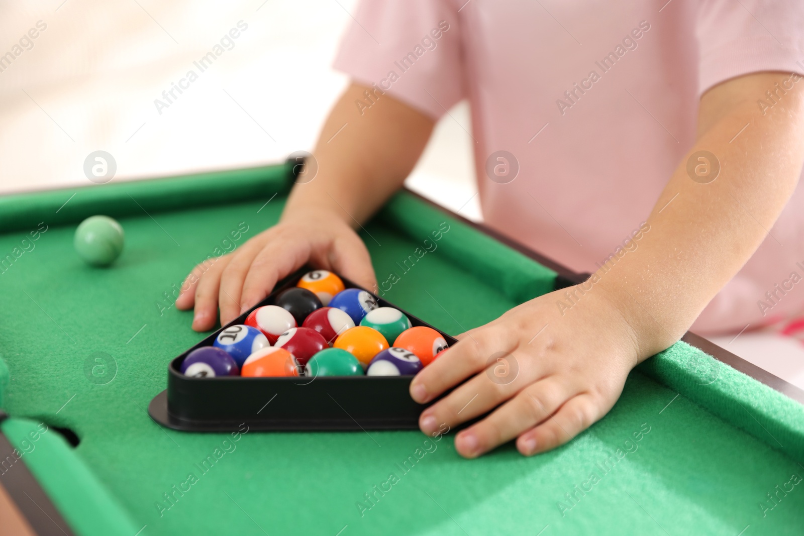 Photo of Little girl with colorful billiard balls in triangle rack at green table, closeup