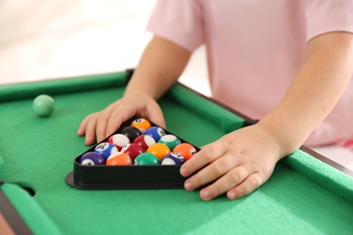 Photo of Little girl with colorful billiard balls in triangle rack at green table, closeup