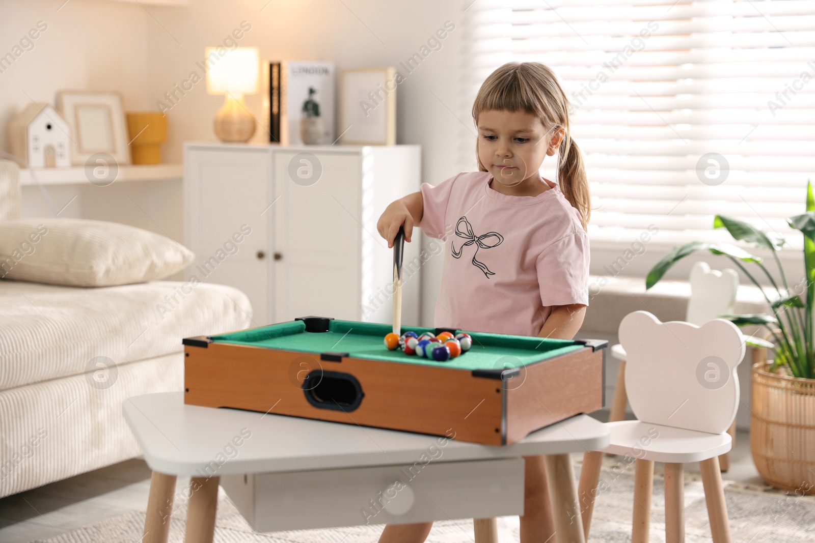 Photo of Cute little girl playing billiards at home