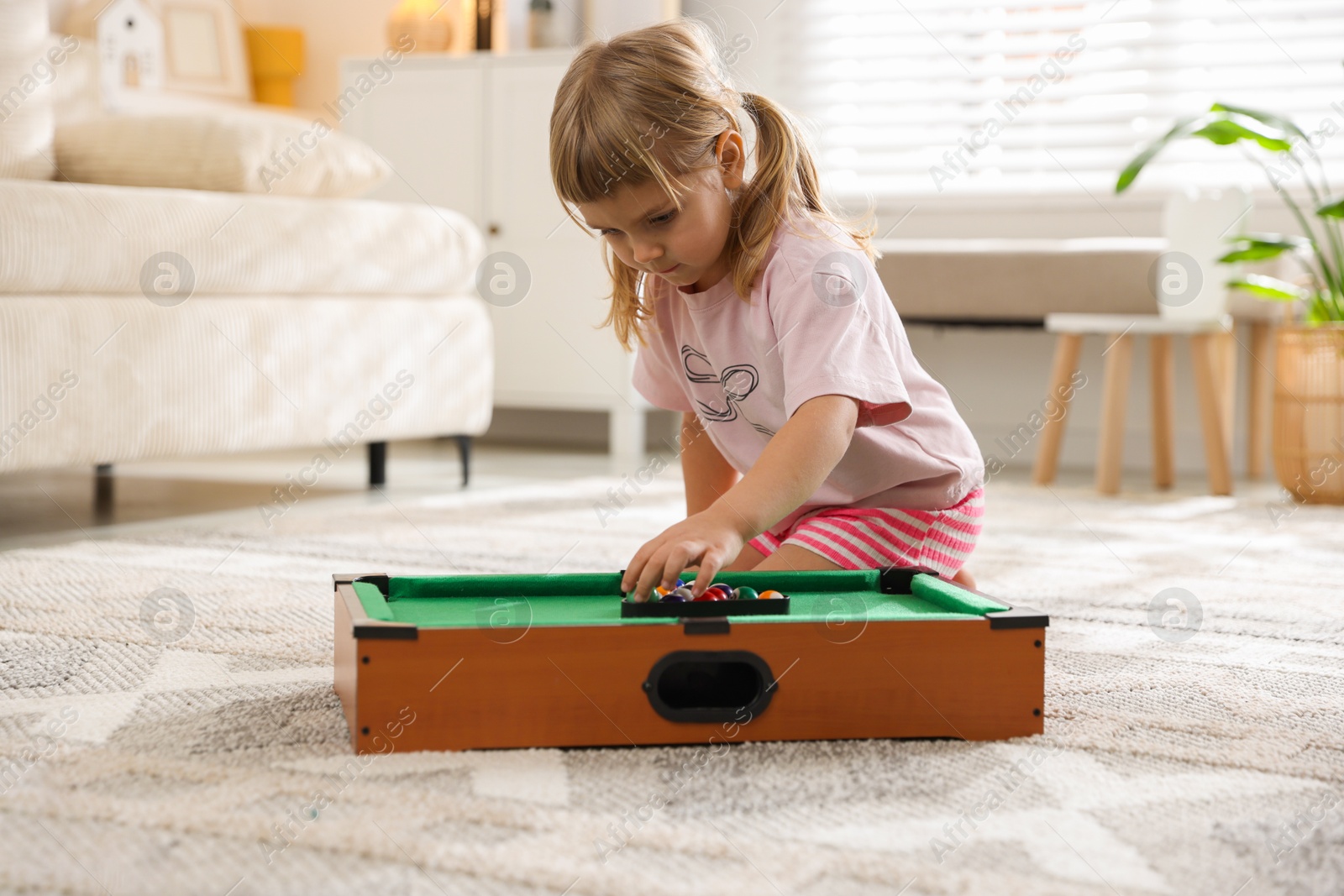 Photo of Cute little girl playing billiards at home