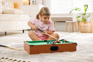 Photo of Cute little girl playing billiards at home