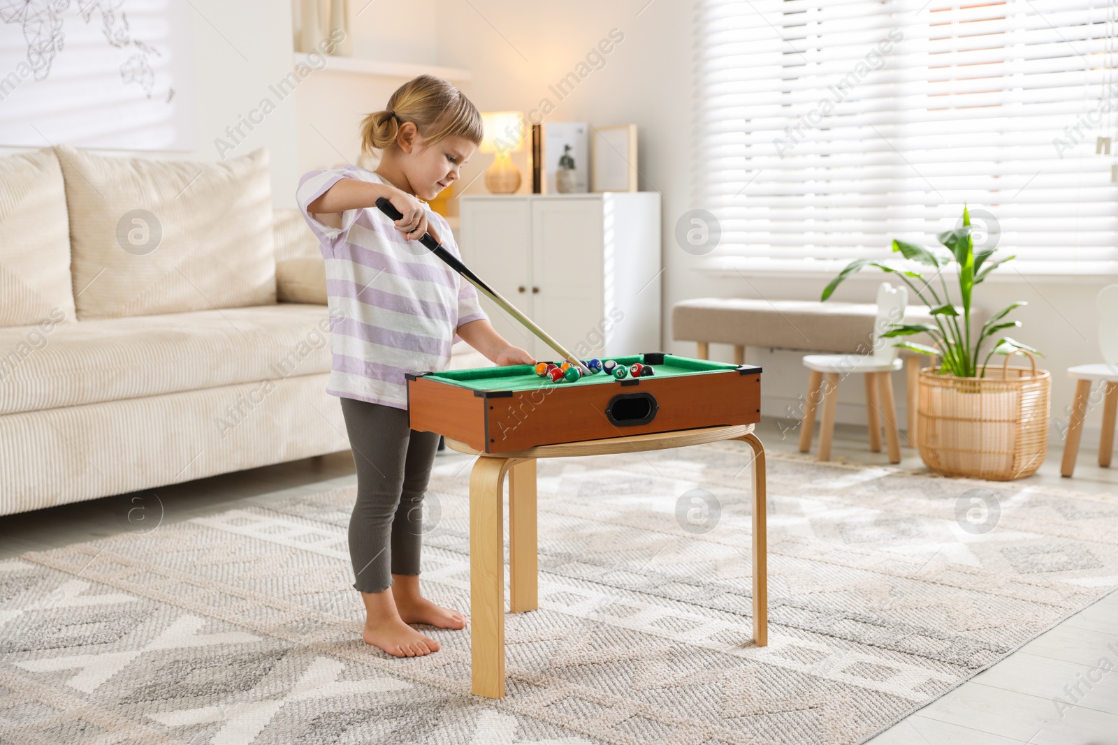 Photo of Cute little girl playing billiards at home