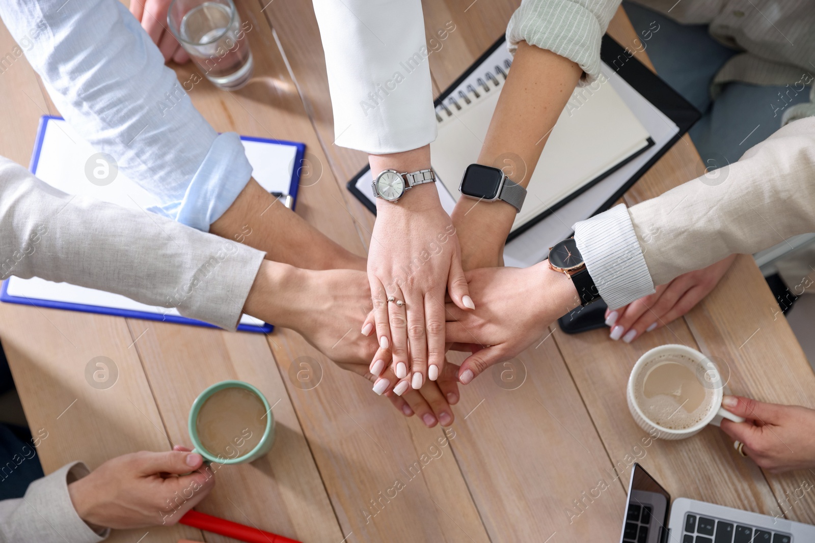 Photo of Unity concept. People holding hands together above wooden table, top view