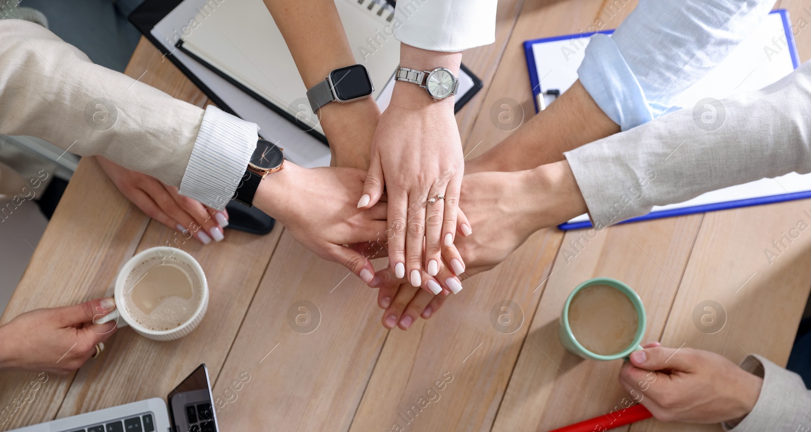 Photo of Unity concept. People holding hands together above wooden table, top view