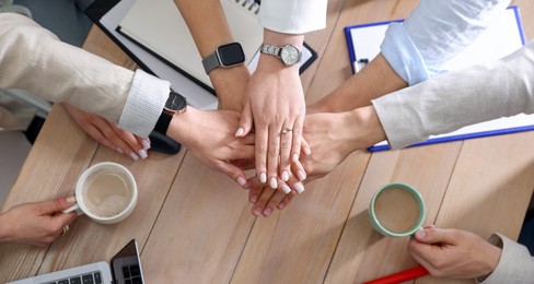 Unity concept. People holding hands together above wooden table, top view