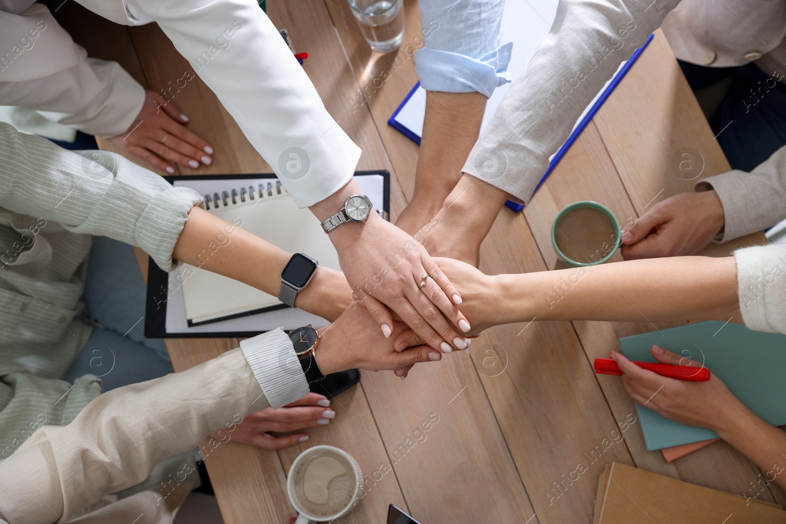 Photo of Unity concept. People holding hands together above wooden table, top view