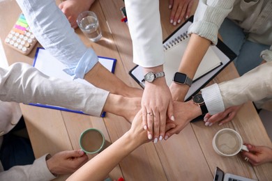 Unity concept. People holding hands together above wooden table, top view