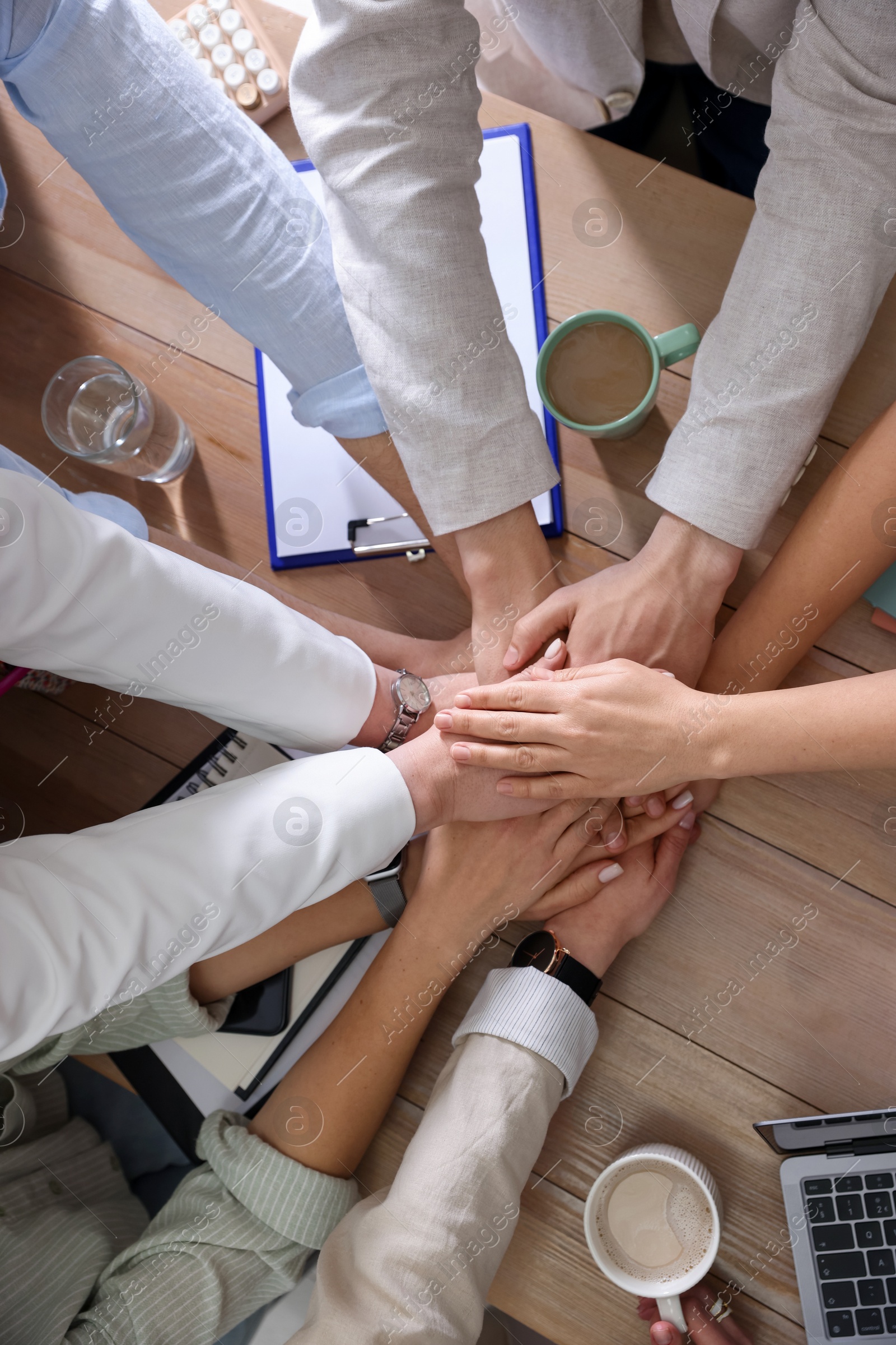 Photo of Unity concept. People holding hands together above wooden table, top view