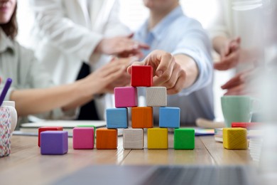 Photo of Unity concept. People building pyramid of colorful cubes at table indoors, closeup