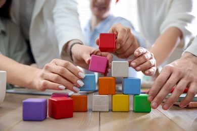 Unity concept. People building pyramid of colorful cubes at wooden table indoors, closeup