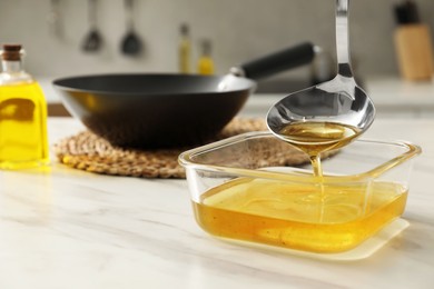 Photo of Pouring used cooking oil into glass container at white marble table, closeup