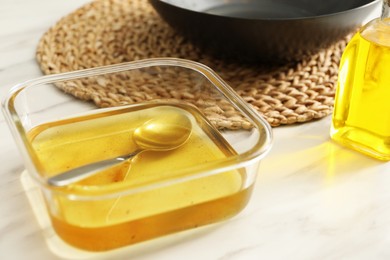 Photo of Used cooking oil and spoon in glass container on white marble table