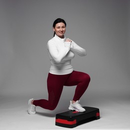 Photo of Plus size woman in gym clothes doing exercise with step platform on grey background