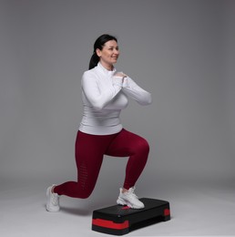 Photo of Plus size woman in gym clothes doing exercise with step platform on grey background