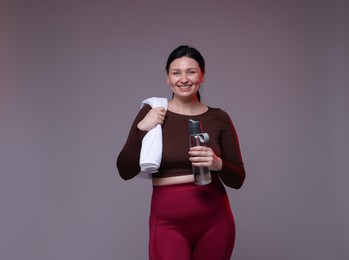 Photo of Plus size woman in gym clothes with water bottle and towel on grey background