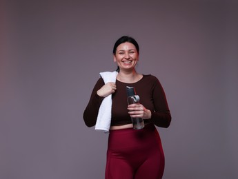 Photo of Plus size woman in gym clothes with water bottle and towel on grey background