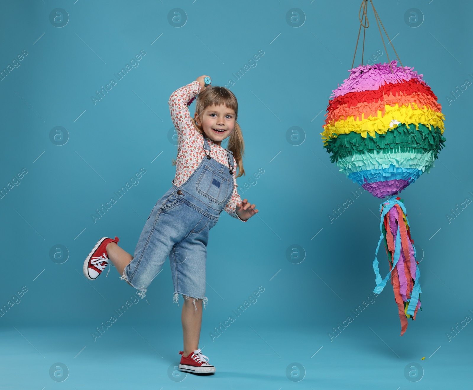 Photo of Happy girl with bright pinata and stick on light blue background