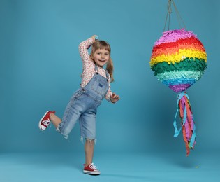 Happy girl with bright pinata and stick on light blue background